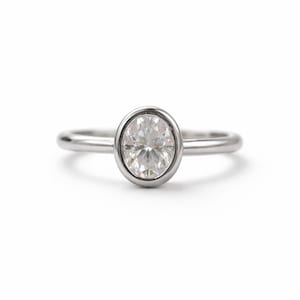 Peut inclure: Une bague en argent avec une pierre précieuse ovale et transparente. La pierre est sertie dans un sertissage à lunette, et le corps de la bague est fin et poli. La bague est présentée sur fond blanc, mettant en valeur son design et son éclat.