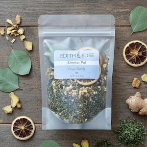 May include: A clear plastic bag of "Edith & Edee" Simmer Pot, "Crisp Clarity" blend, with dried herbs and citrus slices. The bag is surrounded by eucalyptus leaves, ginger pieces, and dried orange slices on a wooden surface.