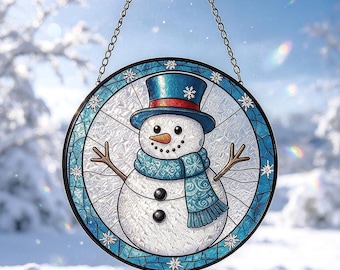 May include: A circular stained glass suncatcher featuring a snowman with a blue top hat, a matching blue scarf, and an orange carrot nose. The design is framed by a blue border with white snowflake accents and hangs from a metal chain.