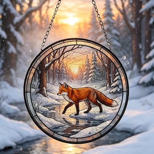 May include: A circular stained glass suncatcher featuring a red fox walking along a snowy stream in a winter forest. The scene is framed by a black metal border and suspended by a metal chain, with a warm sunset glowing through the trees.