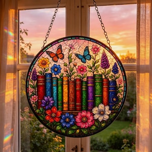 Puede incluir: Un atrapasoles circular de vidrieras que presenta una fila de libros coloridos dispuestos horizontalmente. Sobre los libros hay flores vibrantes y dos mariposas, una naranja y otra azul. La pieza está enmarcada en negro y cuelga de una cadena de metal.