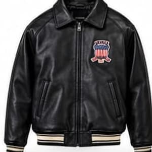 Könnte beinhalten: Eine schwarze Lederjacke mit Frontreißverschluss, spitzem Kragen und zwei Seitentaschen. Die Jacke hat einen Aufnäher auf der linken Brust mit einem rot-weiß-blauen Schildmotiv. Die Ärmelbündchen und der Saum sind mit Streifen versehen.