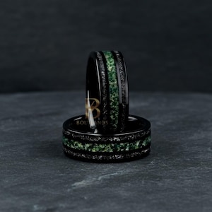 May include: Two black rings with a central band of green speckled material and two outer bands of dark grey speckled material. The rings are set against a dark grey background.