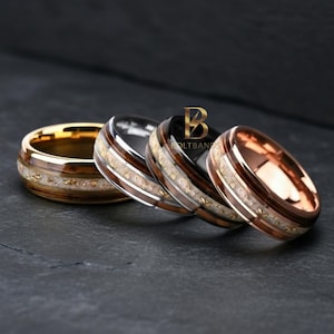 May include: Four rings with unique designs. The rings feature gold, silver, and rose gold bands, with wood grain and speckled inlays. The rings are displayed on a dark surface. The BoltBands logo is visible.