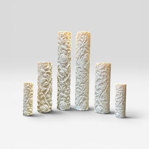 May include: A set of six off-white cylindrical vases of varying heights, each featuring a detailed, raised relief pattern of pomegranate fruits, leaves, and winding vines covering the entire exterior surface of the ceramic vessels.