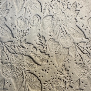 May include: A close-up of a textured, light grey surface with an embossed cherry and leaf pattern. The design features detailed depictions of cherries, leaves, and small floral elements, creating a natural, organic aesthetic.