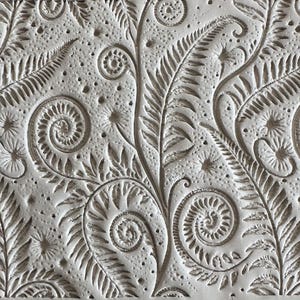 May include: A white textured surface featuring a repeating embossed pattern of fern fronds and curled fiddleheads. The design includes intricate botanical details with deep grooves and small raised dots scattered across the matte white background.
