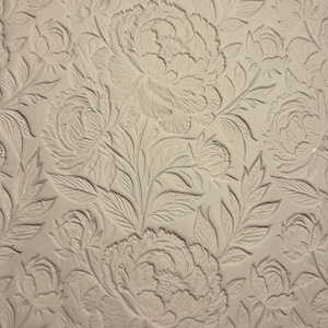 May include: A close-up of a cream-coloured surface with a repeating floral pattern. The design features large, detailed peony blooms and leaves in a raised, embossed style, creating a textured effect.
