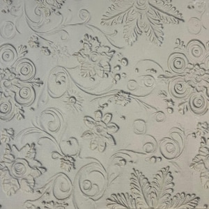 May include: A light grey textured surface featuring a repeating embossed pattern of stylised floral motifs, swirling vines, and circular elements. The design consists of raised, monochromatic shapes that create a tactile, relief-like appearance.