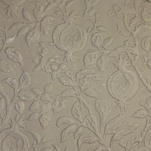 May include: A light beige surface featuring a raised, embossed pattern of pomegranate fruits, leaves, and winding branches. The design is monochromatic, with the relief elements creating subtle shadows and depth across the flat, textured material.