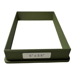May include: An olive green rectangular cookie cutter with a label that reads "5" x 3.5"". The cutter is made of a solid material and has a flat base. The interior is hollow, and the sides are straight.