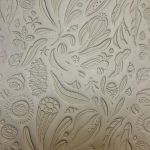 May include: A light beige clay slab featuring a deeply impressed botanical pattern. The surface displays a repeating arrangement of various seed pods, pinecones, elongated leaves, and small star-shaped flowers carved into the textured material.