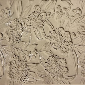 May include: A close-up of a beige floral relief pattern. The design features detailed depictions of flowers, leaves, and buds. The relief creates a textured surface with varying depths, enhancing the visual interest of the botanical theme.