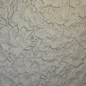 May include: A light grey, flat, rectangular slab of clay featuring a deeply embossed, repeating pattern of hibiscus flowers and tropical leaves. The surface texture is matte and uniform, showcasing intricate floral details in relief.