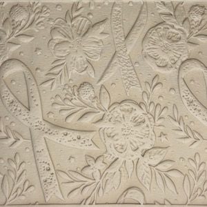 May include: A light beige textured surface featuring an embossed pattern of awareness ribbons interspersed with various floral arrangements, including detailed blossoms, leaves, and small star shapes across the entire flat rectangular area.