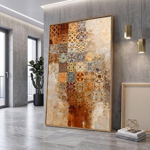 Könnte beinhalten: Ein großes rechteckiges Wandbild mit einer vertikalen Anordnung quadratischer Kacheln, die komplexe geometrische und florale Muster in den Farben gebranntes Orange, Gold, Braun und Creme zeigen, eingefasst in einen dünnen Holzrahmen an einer Betonwand.