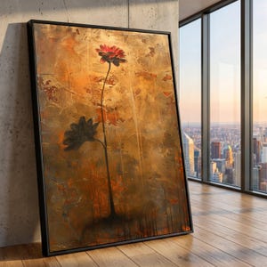 May include: Abstract floral art print in a black frame. The artwork features two stylized flowers, one red and one black, against a textured, golden-brown background. The painting is leaning against a concrete wall, with a city view visible through a window.