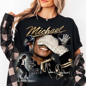 May include: Black t-shirt featuring a collage of images of Michael Jackson, including a portrait, a glove, and a dancing pose. The word "Michael" is written in gold script above the images, with the signature below.