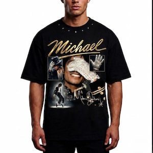 May include: Black t-shirt featuring a gold script of the name "Michael" above a collage of images. The collage includes a portrait, a glove, and a dancing figure. The shirt also has the signature "Michael Jackson" in gold.