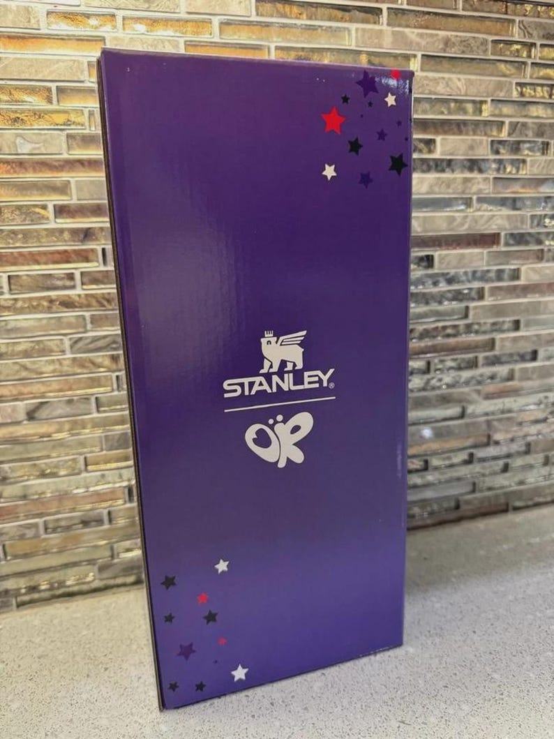 May include: A purple box with the Stanley logo and the letters "OK" in white. The box has a glossy finish and is decorated with red, black, and white stars. The box is rectangular and stands upright.