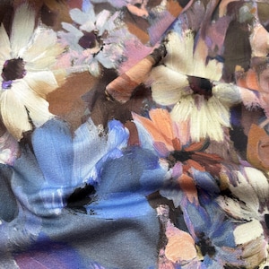 Op de afbeelding: Een stof met een schilderachtig bloemenpatroon met grote, overlappende bloemen in tinten crème, lichtblauw, oudroze en donkerbruin. Het ontwerp heeft zichtbare penseelstreektexturen, wat zorgt voor een zachte, gemengde uitstraling op het textiel.