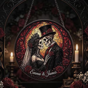 May include: A circular stained glass-style hanging decoration featuring a skeleton couple in wedding attire, including a veil and top hat, surrounded by red roses. The names Emma & James are printed in white script at the bottom of the piece.