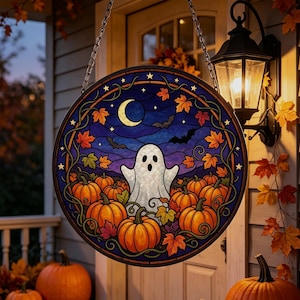 Puede incluir: Una decoración colgante circular de vidrieras que presenta un fantasma blanco entre calabazas naranjas. La escena incluye un cielo nocturno azul oscuro con una luna creciente, estrellas y siluetas de murciélagos, enmarcada por hojas de arce.