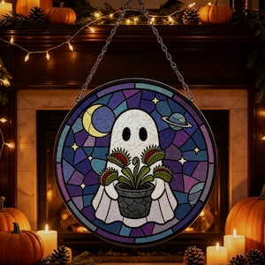 Puede incluir: Un atrapasoles circular de vidrieras que muestra un fantasma blanco sosteniendo una venus atrapamoscas en maceta. El fondo representa un cielo nocturno azul oscuro y morado con una luna creciente amarilla, un pequeño planeta y estrellas.