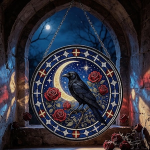May include: A circular stained glass suncatcher featuring a black raven perched on a branch against a crescent moon and starry night sky, surrounded by red roses. The piece is framed by a blue border with red and white cross accents and a chain.