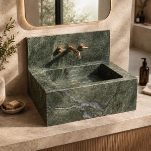 May include: A rectangular forest green marble sink featuring a prominent white veining pattern and a matching stone backsplash. The basin is equipped with a wall-mounted brass faucet assembly consisting of a central curved spout and two handles.