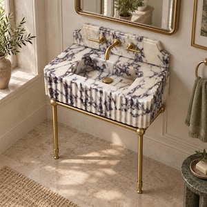 Pode incluir: Um lavatório de casa de banho em mármore branco e roxo com um design exterior canelado, montado num suporte de metal latão. O lavatório inclui uma torneira de latão e dois manípulos de latão, com um painel de mármore integrado na estrutura.