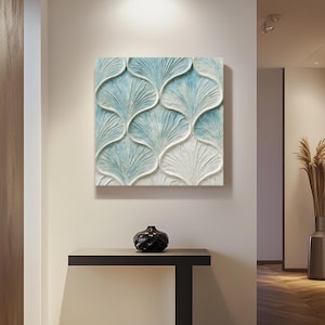 May include: A square wall art piece with a repeating pattern of stylized, light blue and white fan-shaped designs. Below, a black, textured vase sits on a dark, minimalist console table. The scene is set in a well-lit hallway.