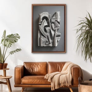 May include: Abstract wooden wall art in a dark brown frame. The artwork features a carved, grey-toned design with organic and geometric shapes. The piece hangs above a brown leather sofa with a beige throw blanket.