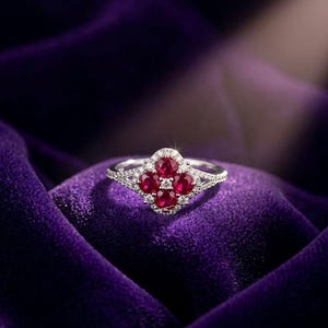 Peut inclure: Une bague en argent avec un motif floral comportant quatre pierres précieuses rondes, rouge foncé au centre. La bague est incrustée de petites pierres précieuses claires et repose sur une surface de velours violet.