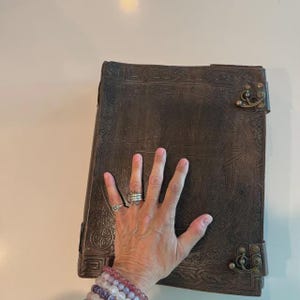 Puede incluir: Un libro grande de cuero marr&oacute;n oscuro con intrincados dise&ntilde;os en relieve, incluyendo una estrella central y patrones geom&eacute;tricos. El libro presenta cierres met&aacute;licos y protectores de esquina.