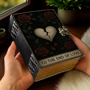 May include: A black book with a broken heart design and red roses. The book has a metal clasp and the text "TO THE END OF LOVE" on the bottom. The pages are aged, and the cover has a gothic aesthetic.
