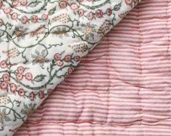 Può includere: Una trapunta reversibile con un motivo floreale su un lato e a righe sull'altro. Il lato floreale presenta fiori rosa e tralci verdi su sfondo bianco. L'altro lato ha strisce orizzontali rosa e bianche. Ideale per letto o divano.