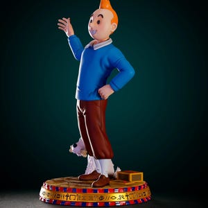 May include: A Tintin figurine featuring the character with orange hair, a blue sweater, and brown trousers, standing on a circular base decorated with Egyptian hieroglyphs. A small white dog is positioned behind the figure on the base.