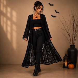 May include: A long, black, open-front crochet cardigan featuring a textured, vertically striped pattern with wide sleeves. The garment is worn over a black tube top, black jeans, and black lace-up boots, creating a cohesive dark ensemble.