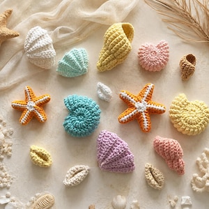 May include: A collection of crocheted sea life figures including various seashells and starfish in shades of white, yellow, light blue, pink, orange, and lavender. The items feature textured yarn stitches and are arranged in a scattered pattern.