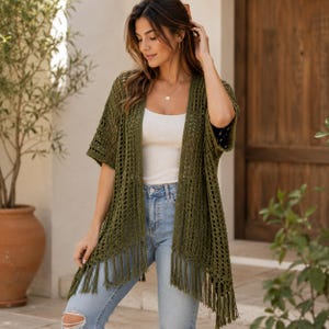 Peut inclure: Un gilet en crochet vert olive ouvert sur le devant, doté d'un motif en maille aérée, de manches courtes et de longues franges le long de l'ourlet inférieur. Le vêtement est porté sur un débardeur blanc simple et un jean bleu clair.