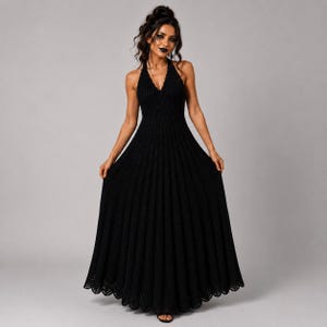 May include: A floor-length black crochet dress featuring a halter neckline, a fitted bodice, and a full, pleated-style skirt with a scalloped hemline. The garment is constructed with a vertical ribbed texture throughout the entire length.