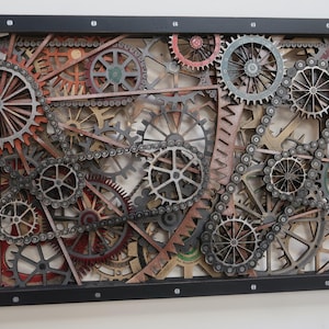 May include: A rectangular wall art piece featuring a complex arrangement of layered wooden gears and metal chains in shades of brown, grey, and red. The mechanical assembly is enclosed within a black frame secured with visible silver screws.