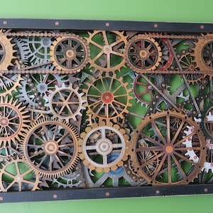 May include: A rectangular wall art piece featuring a complex arrangement of interlocking wooden gears and chains in various shades of brown, gold, and metallic grey, all enclosed within a solid black frame with small metallic accents at the edges.
