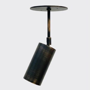 May include: A modern, cylindrical pendant light fixture with a dark bronze finish. The light has a circular ceiling mount and a pivoting head, ideal for directional lighting. The fixture is suspended from a rod.