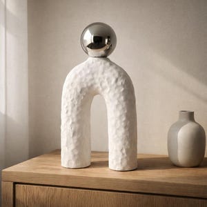 May include: A white ceramic mug with a black handle and the text "But First, Coffee" in a bold, black font. The mug is set against a blurred background, suggesting a cozy setting.