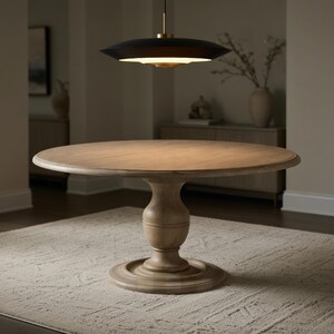 May include: A round wooden dining table with a pedestal base. The table is light brown and sits on a patterned rug. A black and gold pendant light hangs above the table, illuminating the surface. The table is approximately 48 inches in diameter.