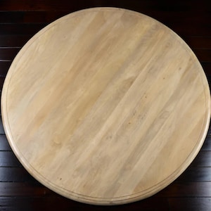 May include: A round wooden table top with a light, natural wood finish. The table top has a diameter of approximately 48 inches and features a subtle, decorative edge. The wood grain is visible, adding to the table's rustic charm.