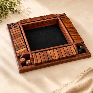May include: A wooden Shut the Box dice game. The game board is square with a dark felt center and numbered wooden tiles. Dice are visible in the game's compartments. The wood has a rich, warm tone.