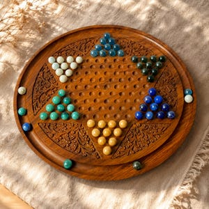 May include: A wooden Chinese checkers board with carved floral designs. The board is round with holes and holds colorful marbles in blue, green, yellow, and white. The game board is set on a tan surface.